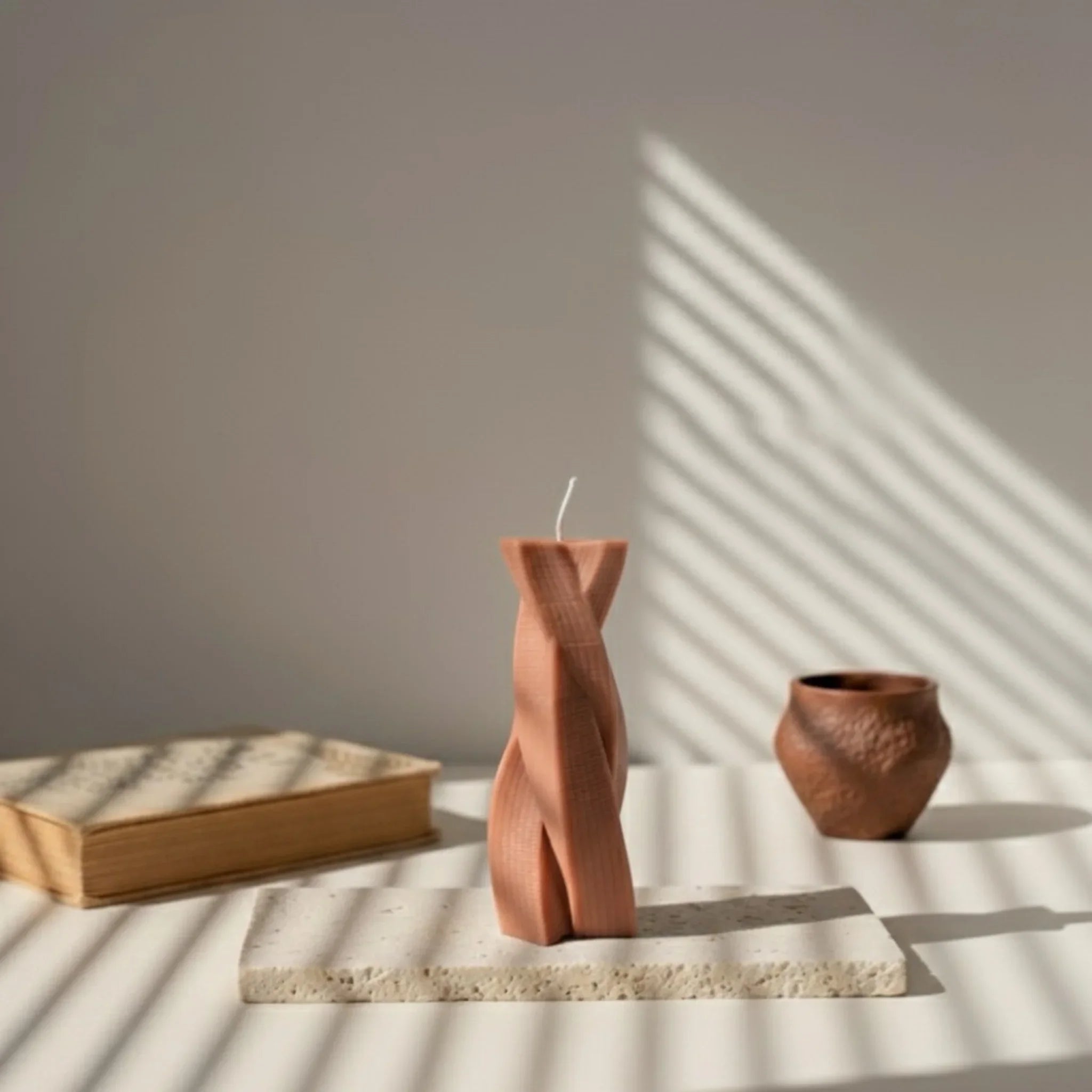 Bougie design torsadée terracotta sur plateau, décor minimaliste éclairé par la lumière naturelle