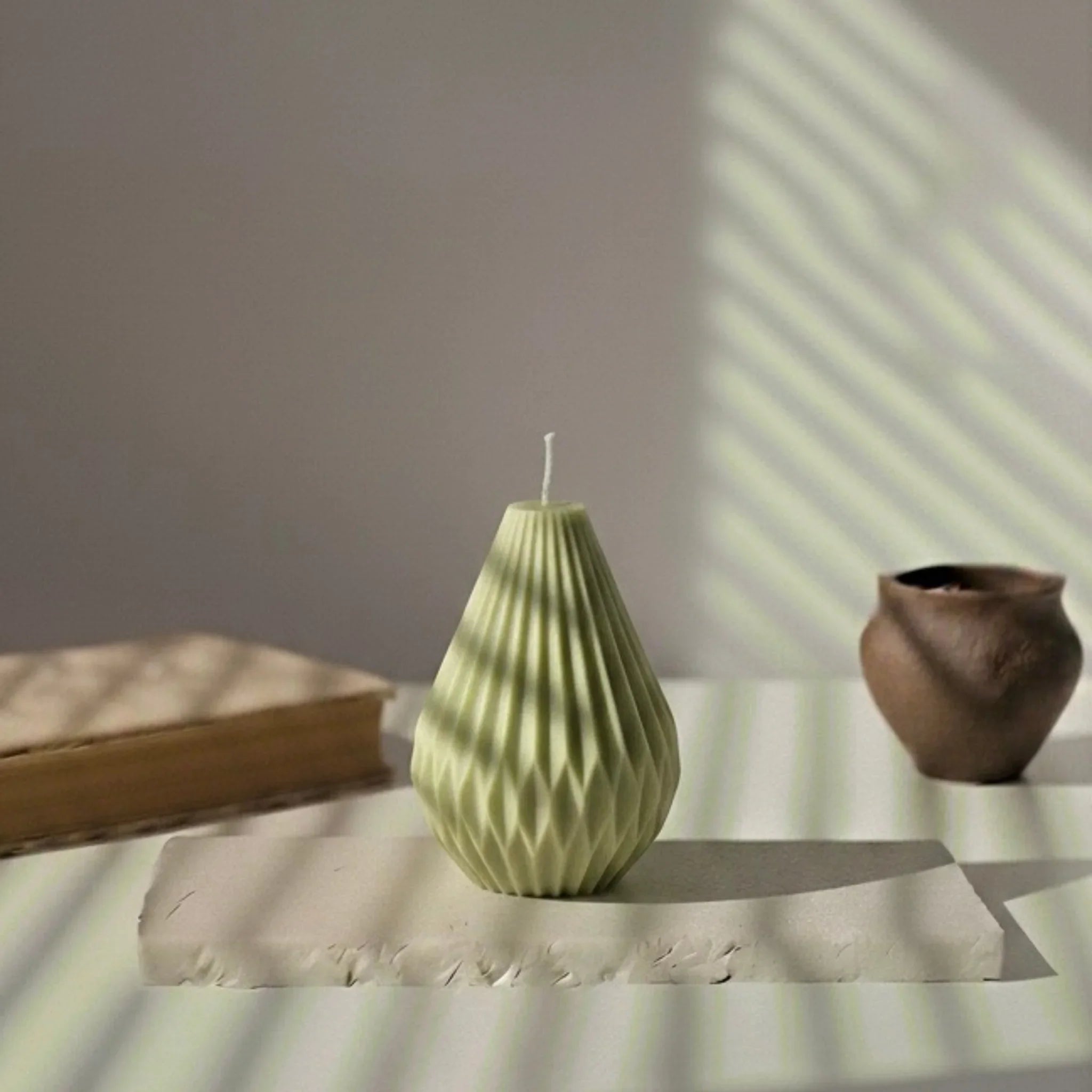Bougie décorative vert kaki en forme de montgolfière sur table, lumière naturelle, style artisanal.