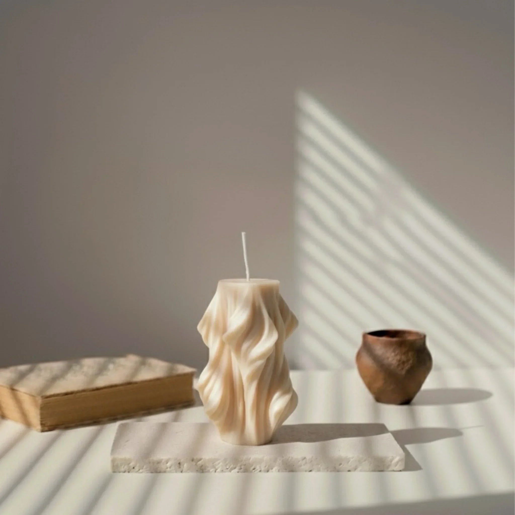 Bougie décorative blanche ondulée sur table minimaliste, L'Atelier Rochelais, lumière naturelle