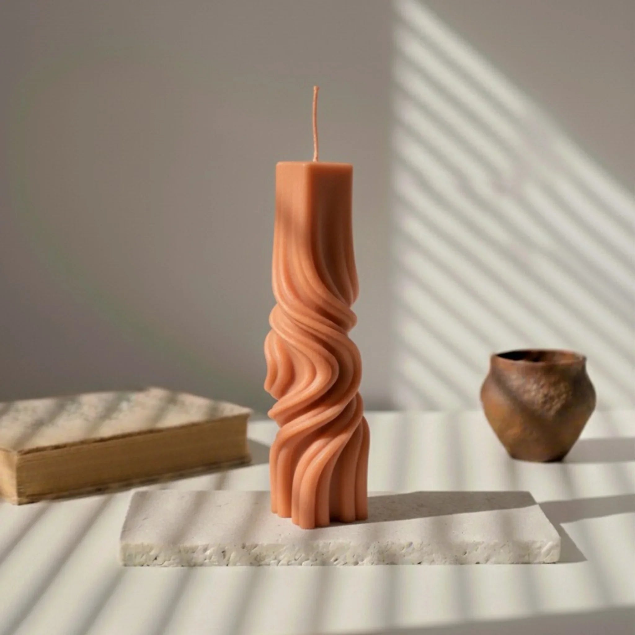 Bougie totem décorative terracotta à motifs torsadés, posée sur une table minimaliste.