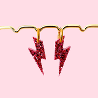 Boucles d’oreilles artisanales éclairs rouges pailletés L’Atelier Rochelais sur fond rose