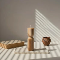 Bougie design marron en cire nervurée sur socle, décor minimaliste, lumière naturelle.