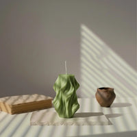 Bougie décorative verte kaki wavy sur table, lumière naturelle, style minimaliste.