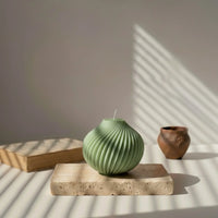 Bougie décorative sphérique vert kaki posée sur une pierre, lumière naturelle, L'Atelier Rochelais