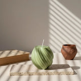 Bougie spirale design vert kaki sur support en pierre, déco élégante, lumière naturelle.